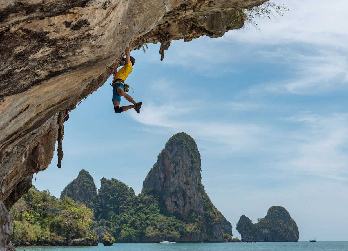 Rock climber leading a gorgeous orange limestone cliff face next to the blue ocean